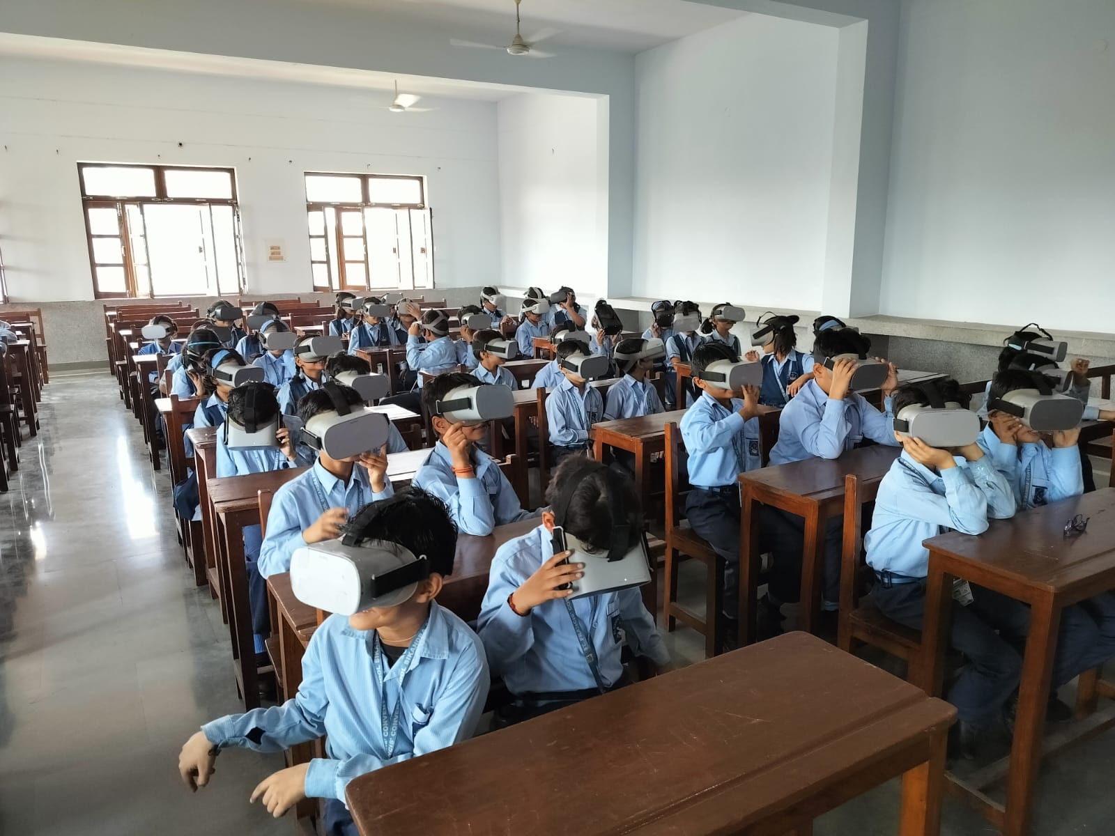 A classroom of students wearing virtual reality headsets during an educational VR session, exploring immersive digital content while seated at their desks in a school environment.